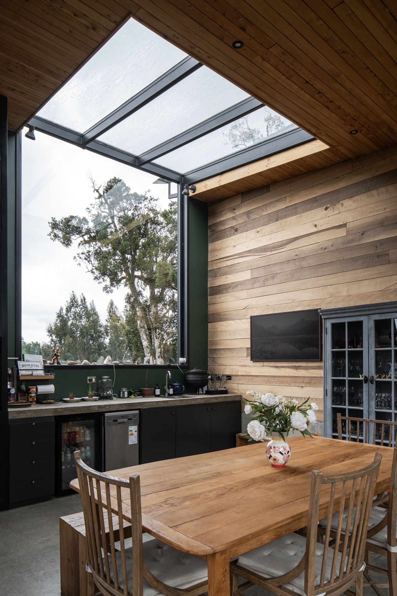 Gran ventana del quincho, paisaje nativo y muro de madera de laurel. Casa Carpintero. LAGAR arqtos.